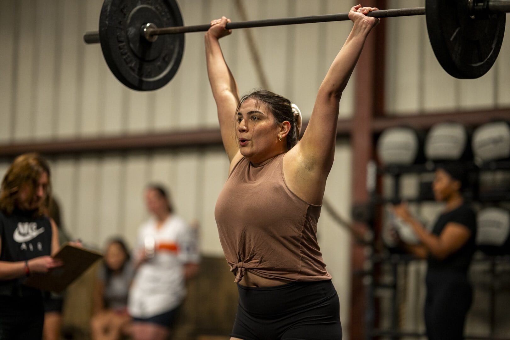 A beautiful woman pushes a loaded barbell overhead during one of her workouts at the gym in Independence Heights.